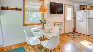 A modern kitchen with a dining table, chairs, a TV, and a refrigerator. - Secluded Ozark Mtn Cottage w/ Wraparound Deck (Eureka Springs)