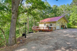A yellow cabin with a red roof, surrounded by trees, and a gravel driveway.