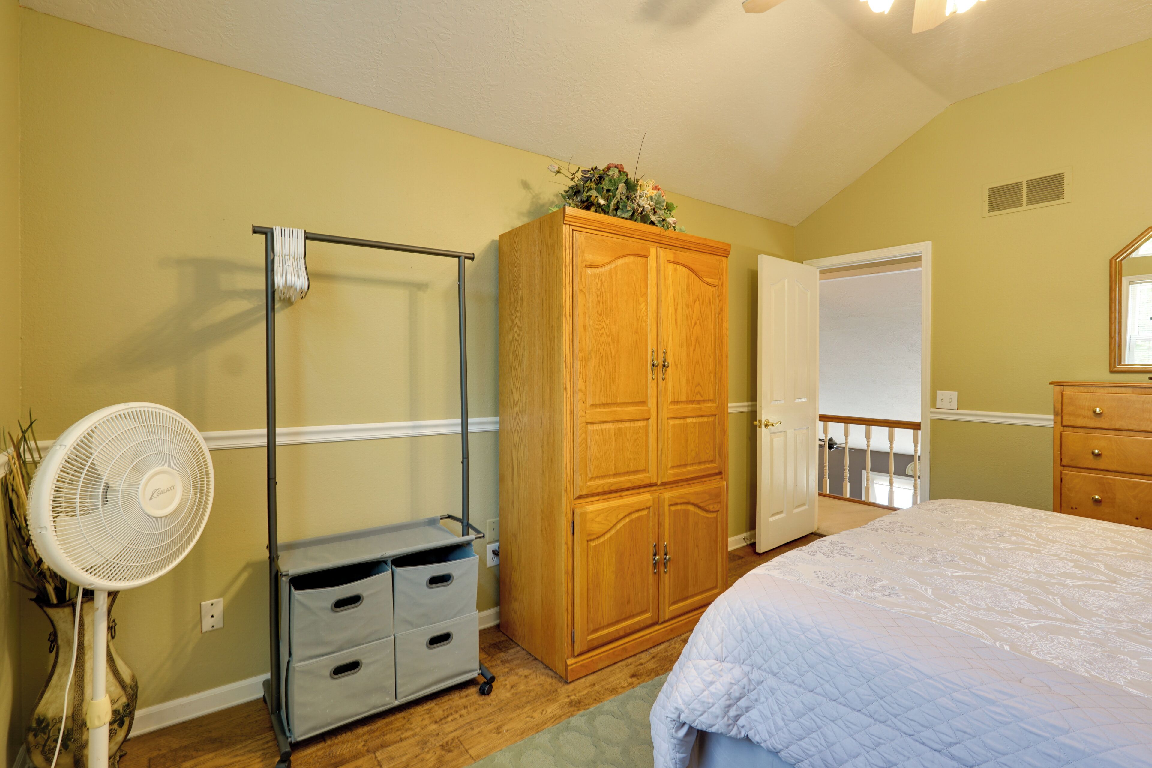 Une chambre à coucher comprenant un lit, une armoire, un ventilateur et une porte donnant sur un balcon.