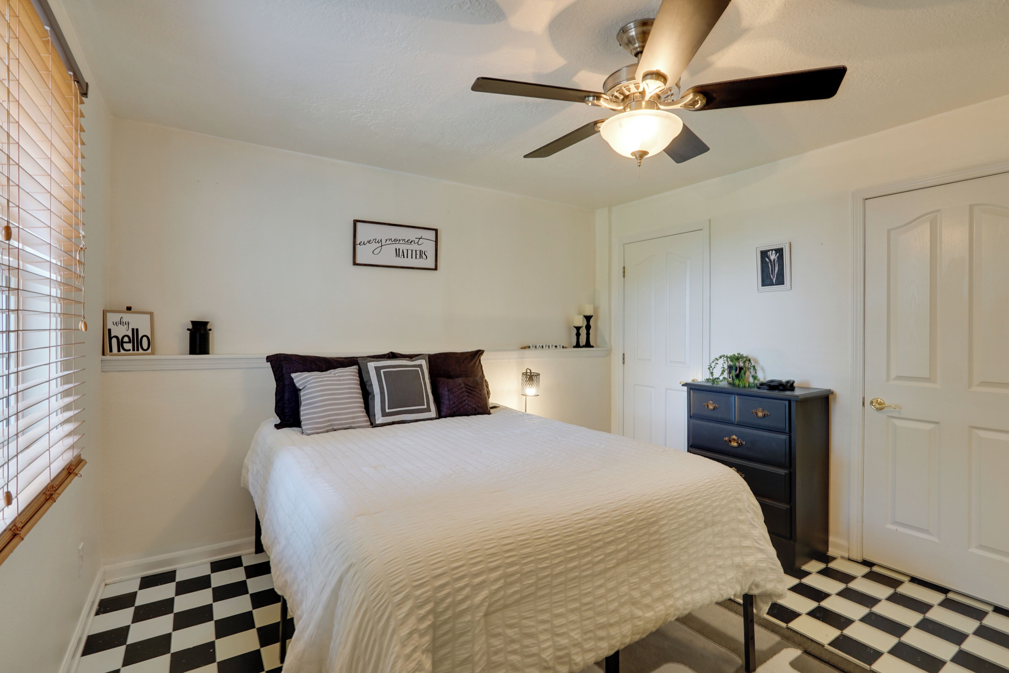 A bedroom with a bed, a dresser, a ceiling fan, and a door.