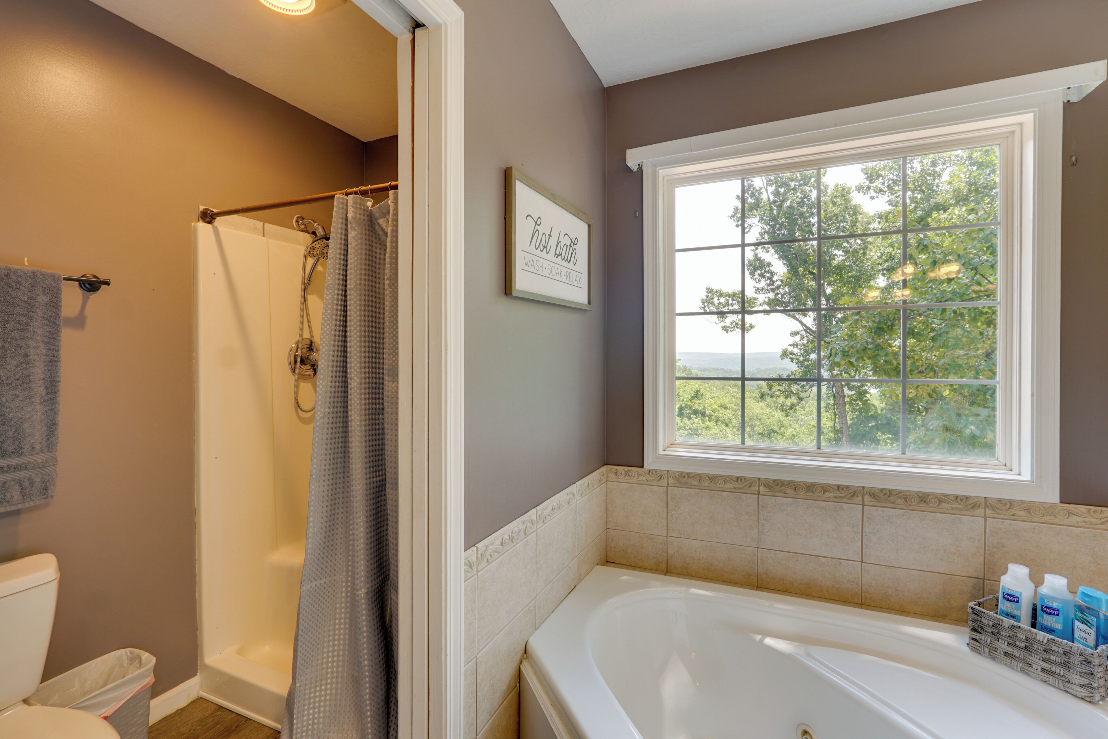 A bathroom with a bathtub, shower, and a window with a view of trees.