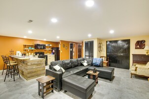 Una sala de estar moderna con un sofá de cuero negro, una isla de madera con taburetes de bar, una mesa de comedor y una zona de cocina con microondas y estufa.