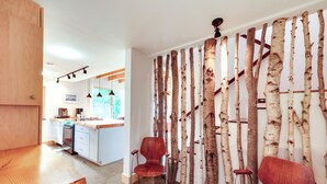 A modern kitchen with white cabinets, a wooden countertop, and a dining area with two red chairs. - Acadia Home w/ Rooftop Deck - Close to Trails! (Mount Desert)