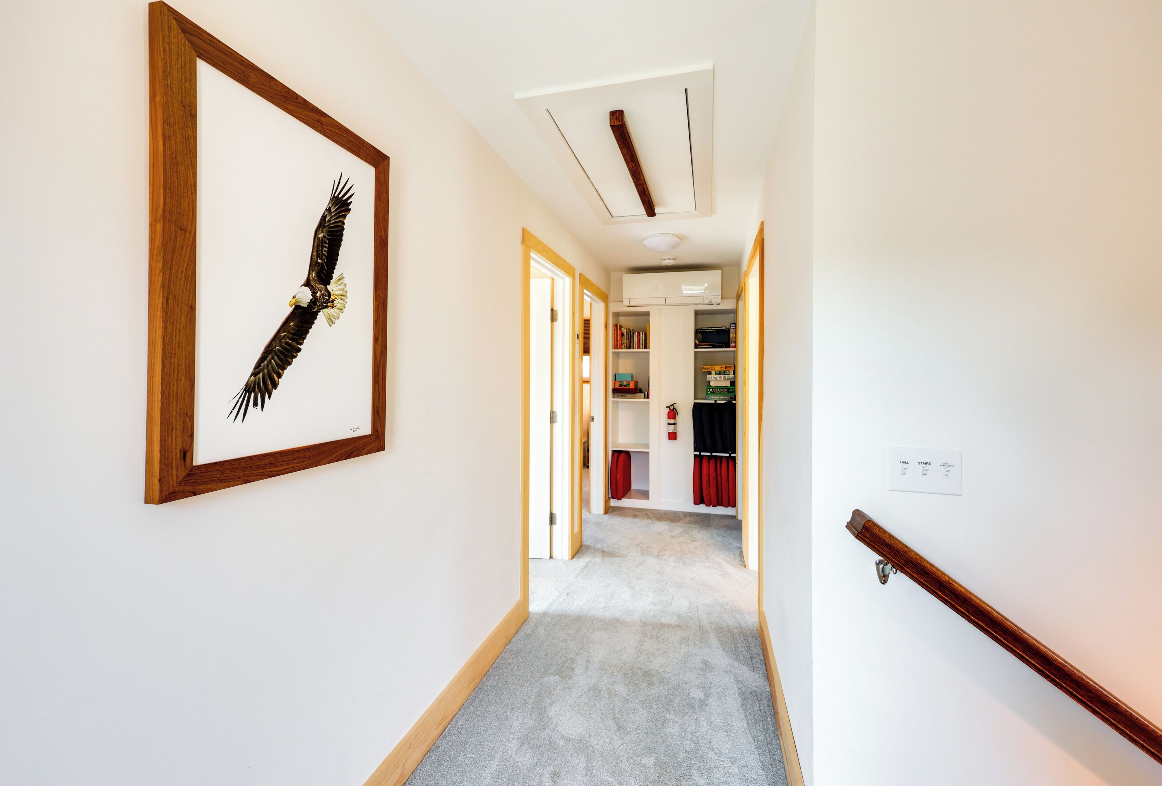 A hallway with a framed eagle artwork, a wooden handrail, and a ceiling with recessed lighting.