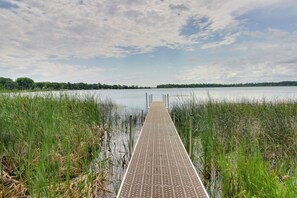 Un muelle de madera se adentra en un lago tranquilo bordeado por altas hierbas.