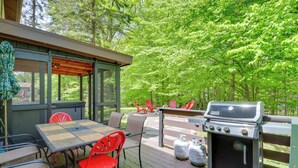 An outdoor deck with a grill, red chairs, and a table. - Private Hot Tub & Fire Pit: Pocono Lake House! (Pocono Lake)