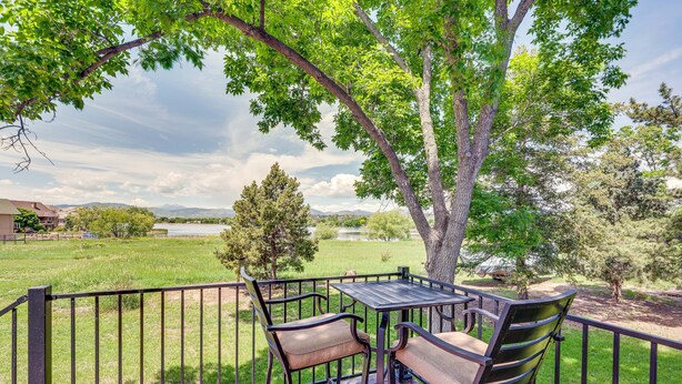 Une terrasse avec une table et des chaises, donnant sur un espace verdoyant agrémenté d’arbres et offrant une vue lointaine sur les montagnes.