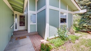 Une maison à l’extérieur verdoyant, avec une porte d’entrée et un petit jardin devant, agrémenté de plantes et d’un paillasson.