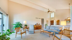 Un salon spacieux doté d’une grande fenêtre, d’un ventilateur de plafond et de différents types de sièges, notamment un canapé, des fauteuils et une table basse.