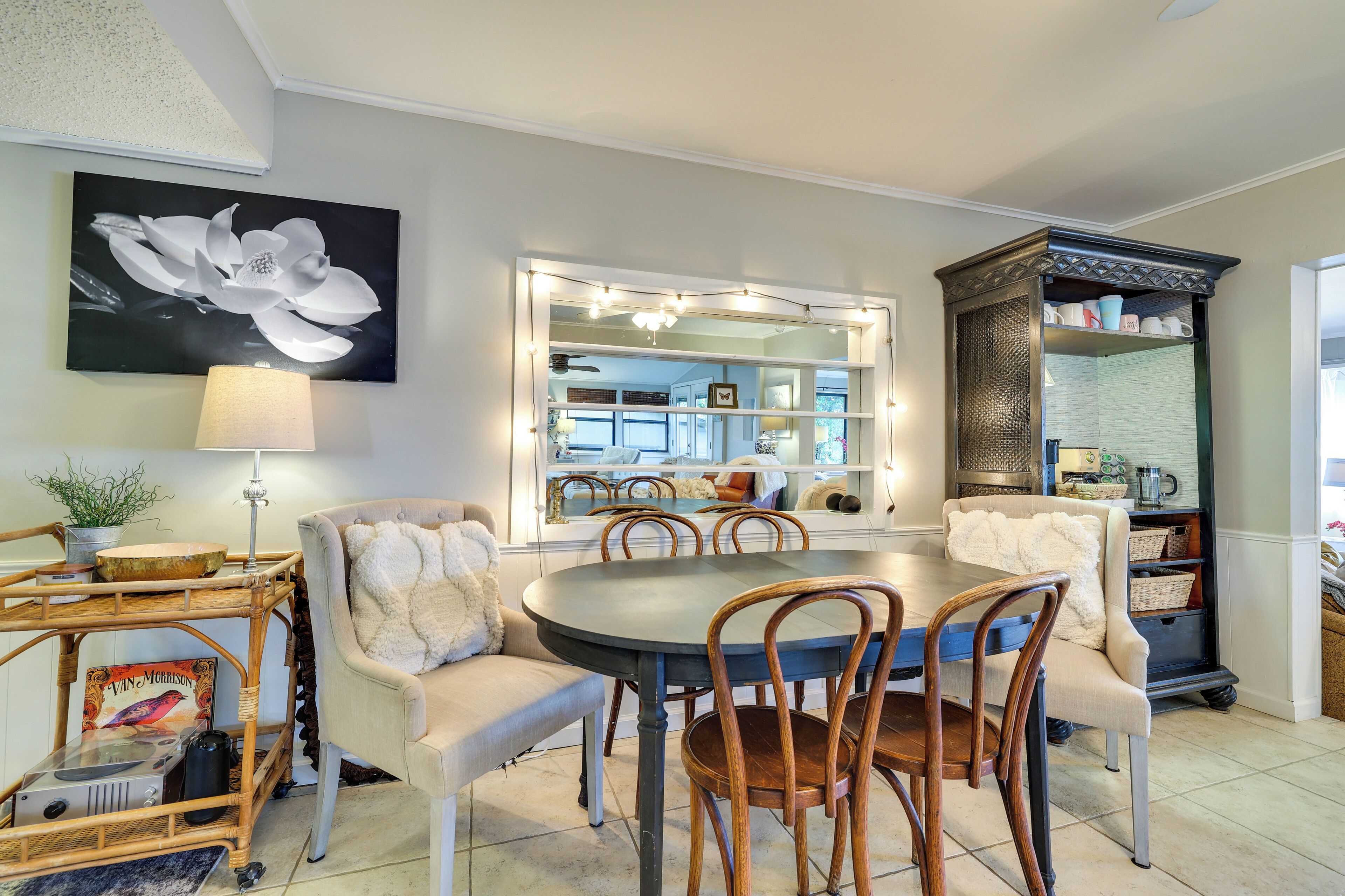 Un coin repas avec une table ronde, des chaises, une lampe, une bibliothèque et un grand miroir.