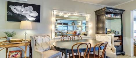 Un coin repas avec une table ronde, des chaises, une lampe, une bibliothèque et un grand miroir.