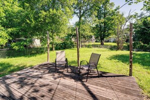 A wooden deck with two chairs, surrounded by trees and a grassy area.