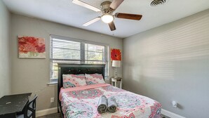 Ein Schlafzimmer mit Bett, Deckenventilator, Fenster mit Jalousien und Schreibtisch.
