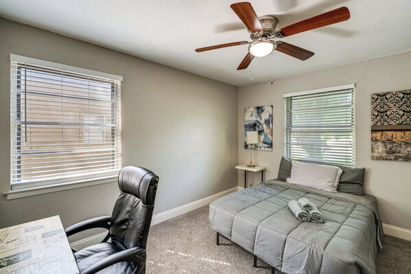 A bedroom with a bed, a chair, a ceiling fan, and two windows with blinds.