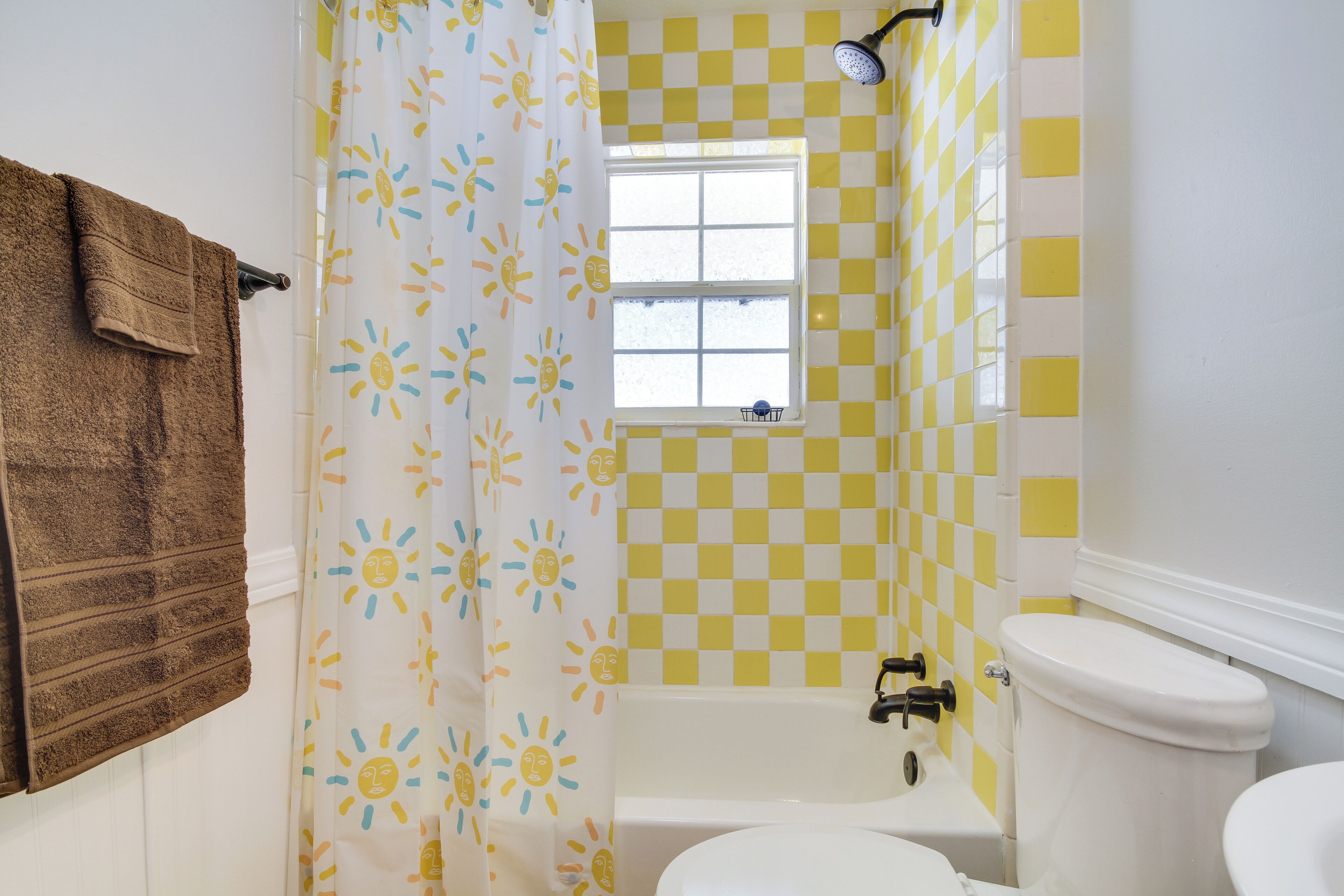 Casa de banho com parede xadrez amarelo e branco, banheira branca, sanita branca e cortina de chuveiro com padrão de sol.