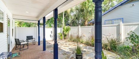 Une terrasse couverte avec un sol en briques, des meubles d’extérieur et des plantes en pot.