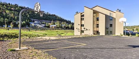 Un bâtiment devant lequel se trouve un terrain de basket-ball, le tout étant entouré d’une zone recouverte de gravier et de verdure.