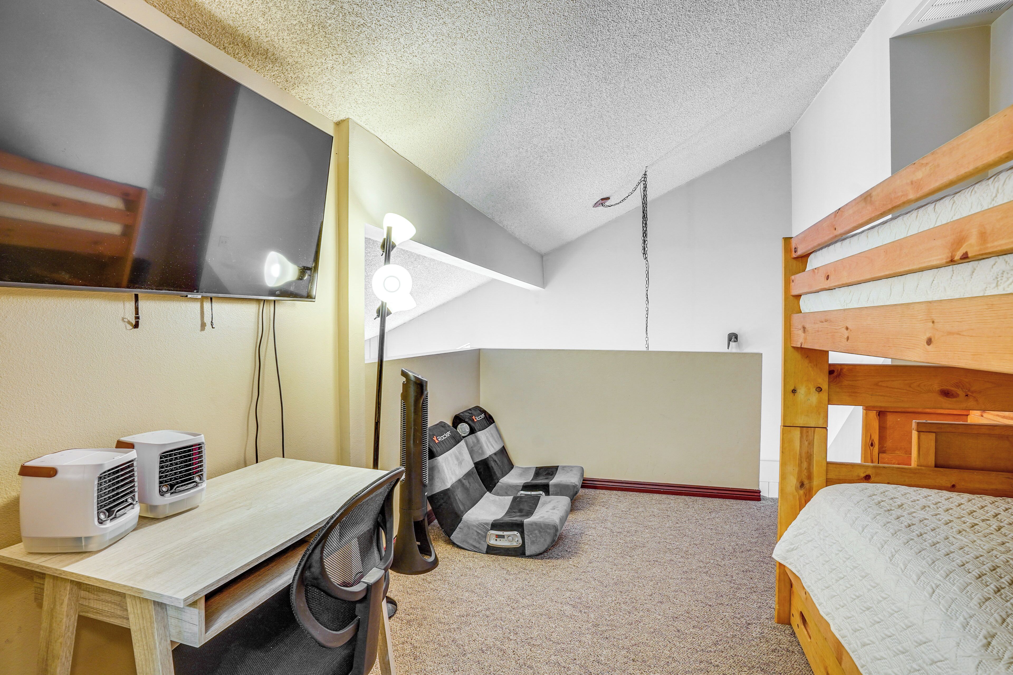 A compact room with a bunk bed, a desk with a chair, two air purifiers, a standing heater, and a ceiling fan.