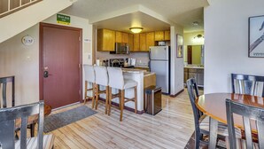 A compact kitchen with wooden cabinets, a microwave, and a refrigerator. There is a dining area with a small table and chairs. - Ski-in/ski-out Brian Head Condo w/ Hot Tub! (Brian Head)