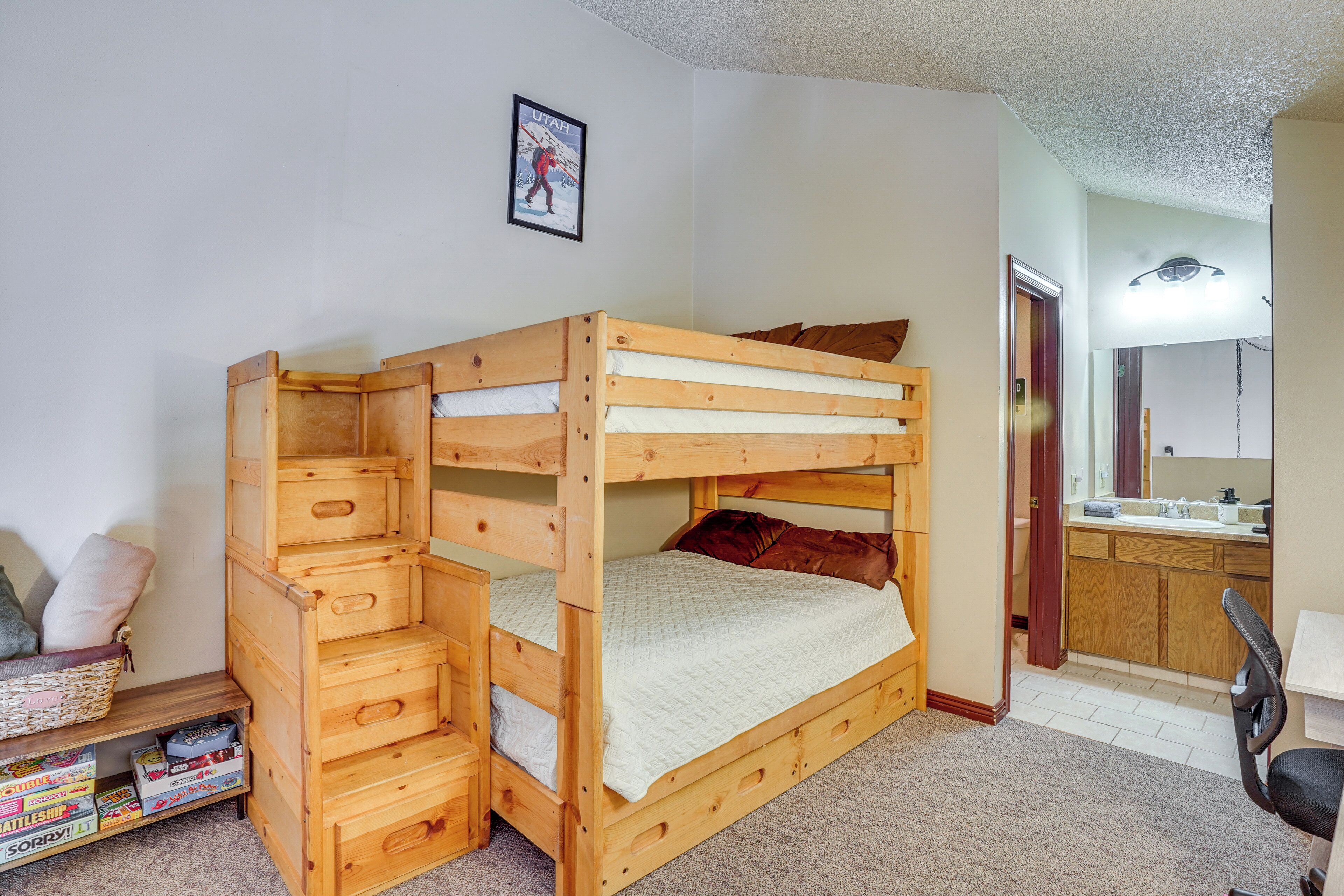 A bunk bed with storage drawers, a small desk, and a bathroom with a sink and mirror.