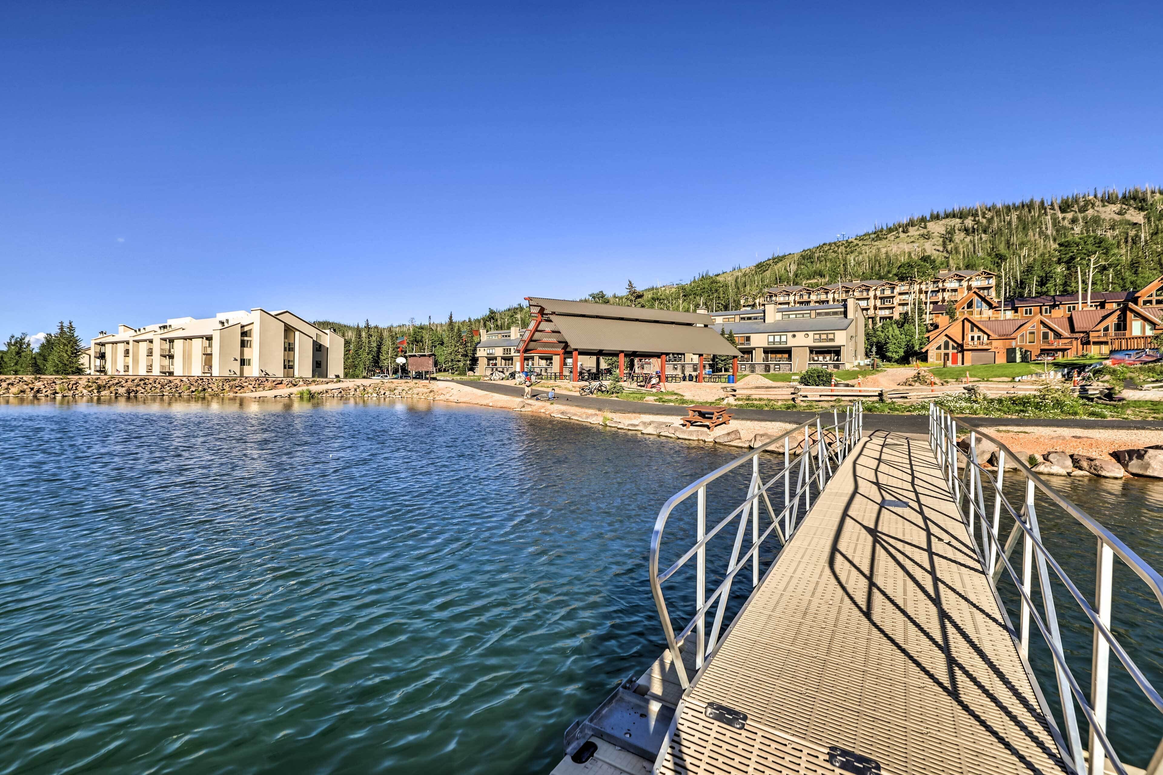 A waterfront hotel with a dock, buildings with a modern architectural style, and a backdrop of a forested hillside.