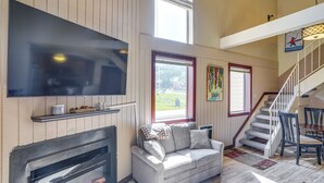A spacious living area with a fireplace, a large flat-screen TV, a sofa, and a staircase leading to an upper level. - Ski-in/ski-out Brian Head Condo w/ Hot Tub! (Brian Head)