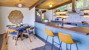 A modern kitchen with a central island, wooden chairs, and a hanging light fixture. - Whidbey Island Oasis: Walk to Beach, Hot Tub, View (Greenbank)