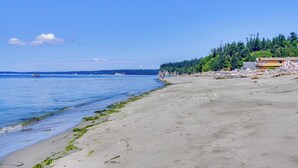 A beach with clear blue water, a sandy shore, and a forested hill in the background. - Whidbey Island Oasis: Walk to Beach, Hot Tub, View (Greenbank)