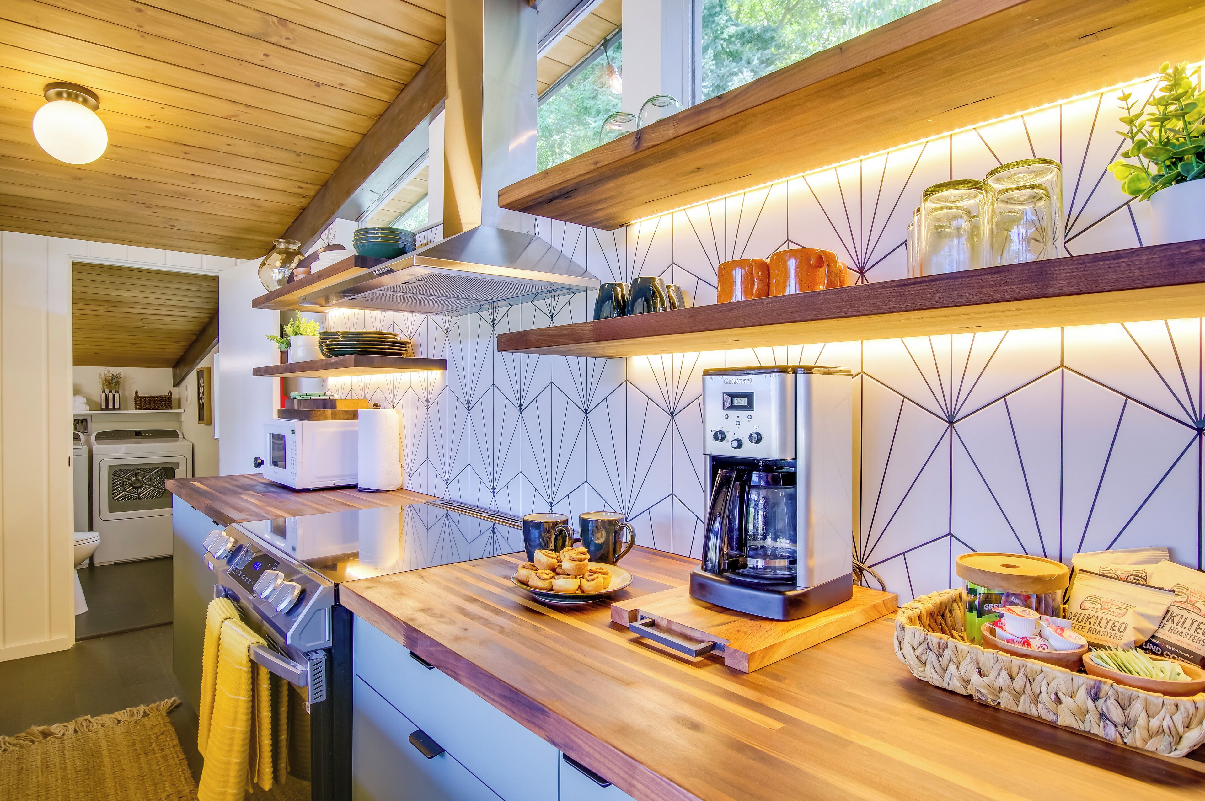 A modern kitchen with wooden countertops, a coffee maker, and a variety of kitchenware on shelves.
