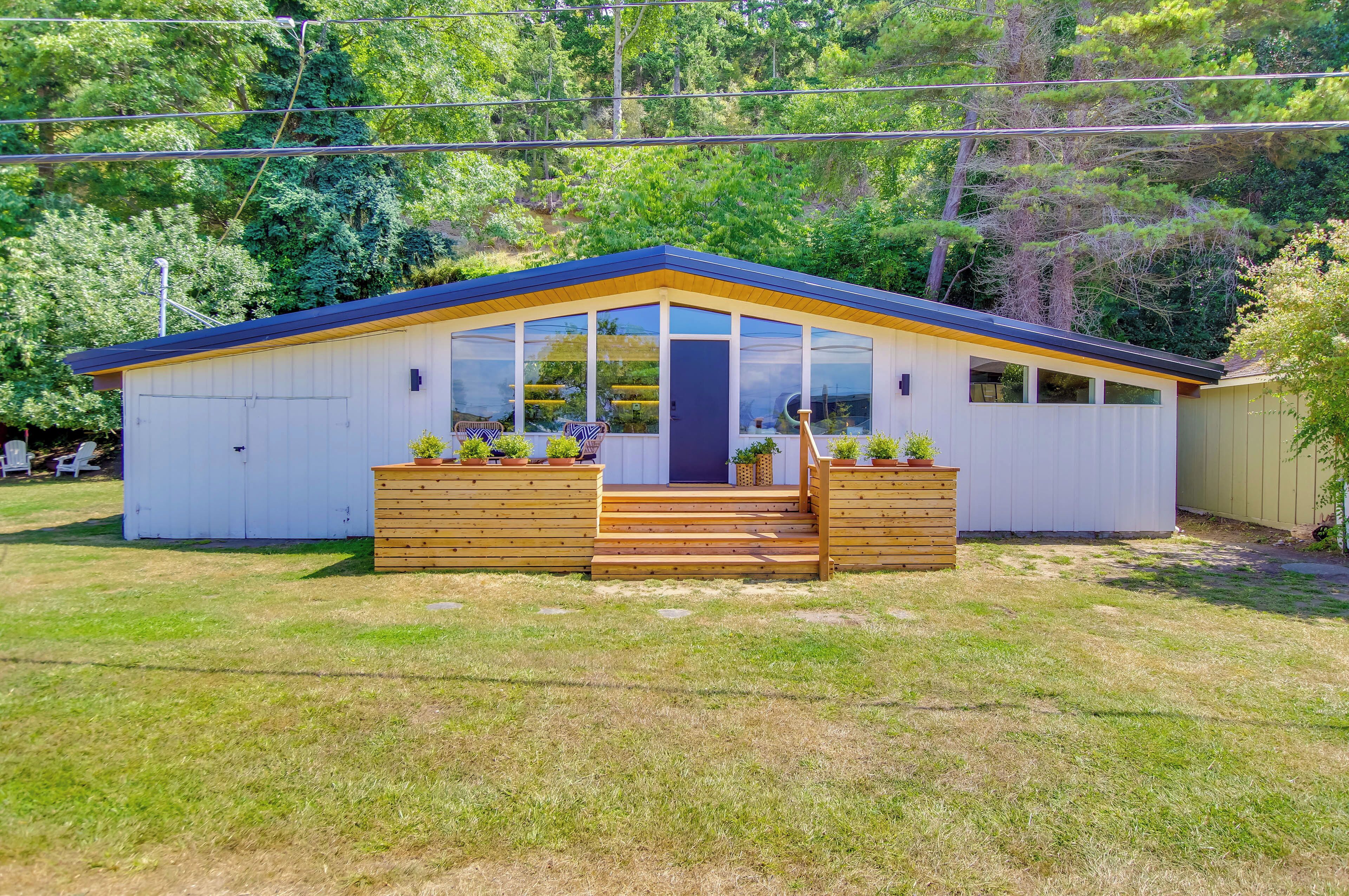 A small, single-story building with a blue roof and large windows, surrounded by a grassy area and trees.