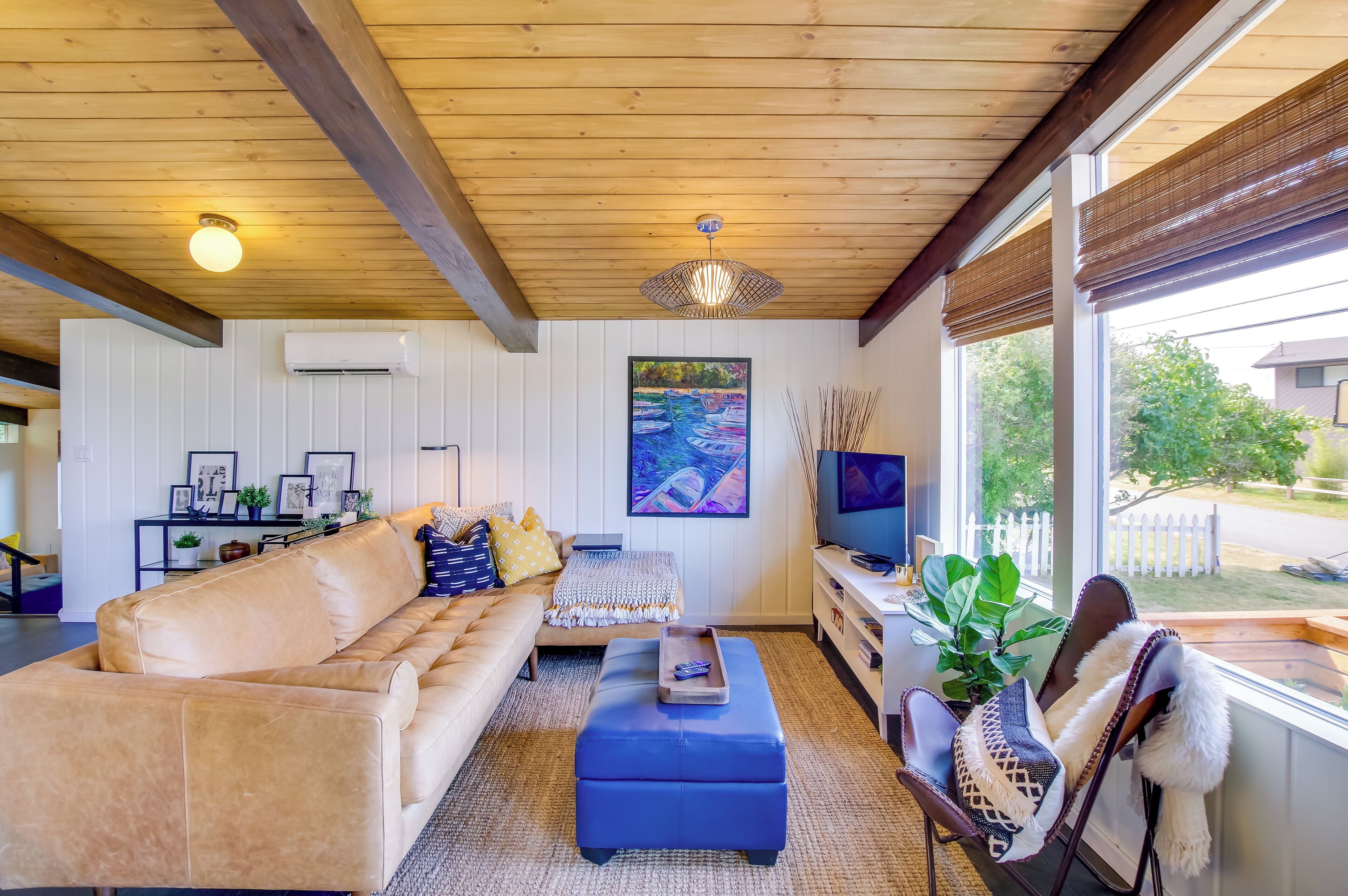 A living room with a beige sofa, a blue ottoman, a TV, and a painting on the wall.