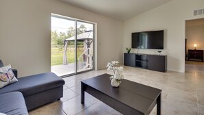 A spacious living room with a sliding glass door leading to a patio, a flat-screen TV mounted on the wall, a dark coffee table, and a gray sofa. - Lake Wales Vacation Rental Near Lake Kissimmee! (Lake Wales)