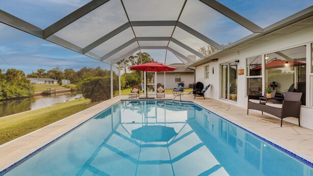 A swimming pool with a covered patio area, outdoor furniture, and a view of a lake. - Riverfront Florida Retreat w/ Pool, Patio & Grill! (Port Charlotte)
