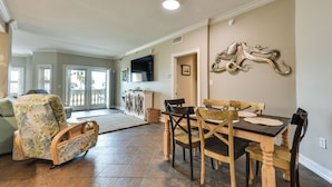 A dining area with a wooden table and chairs, a sofa with a leaf-patterned cover, and a wall-mounted decorative piece. - Pet-friendly Fernandina Beach Condo: Walk to Beach (Fernandina Beach)