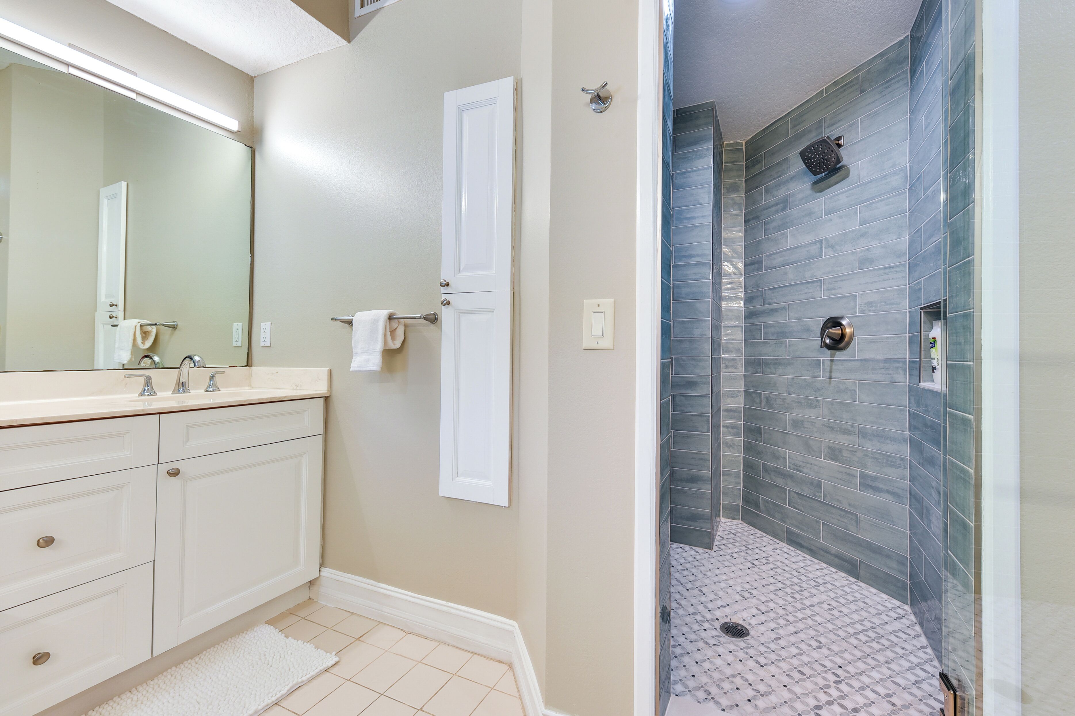 A bathroom with a white vanity, a large mirror, and a shower with blue tiles.