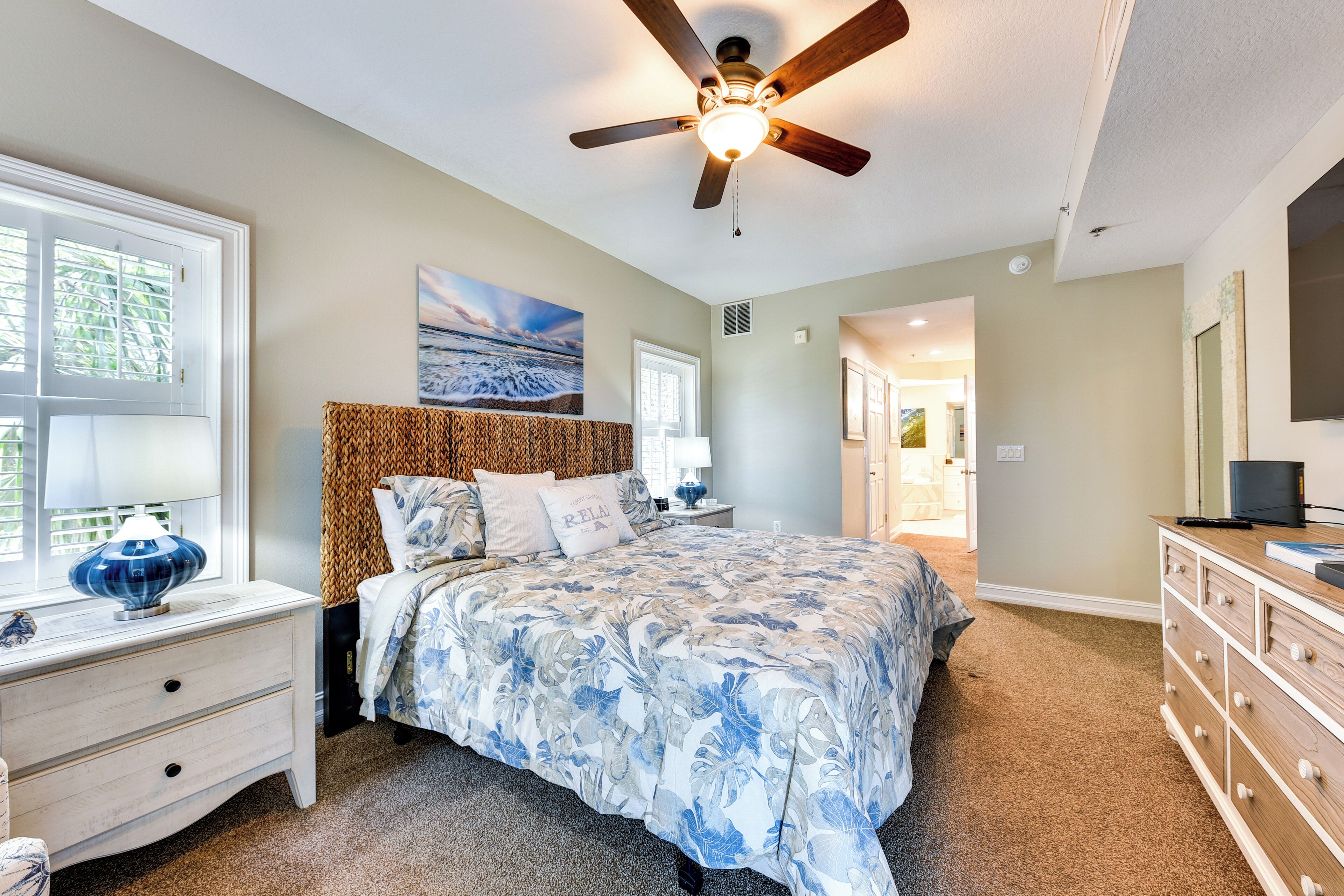 A bedroom with a bed, a nightstand, a dresser, a ceiling fan, and a painting on the wall.