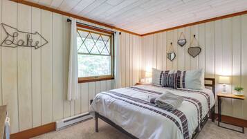 A bedroom with a bed, a nightstand, a window with curtains, a wall-mounted sign, and a wall with decorative mirrors.