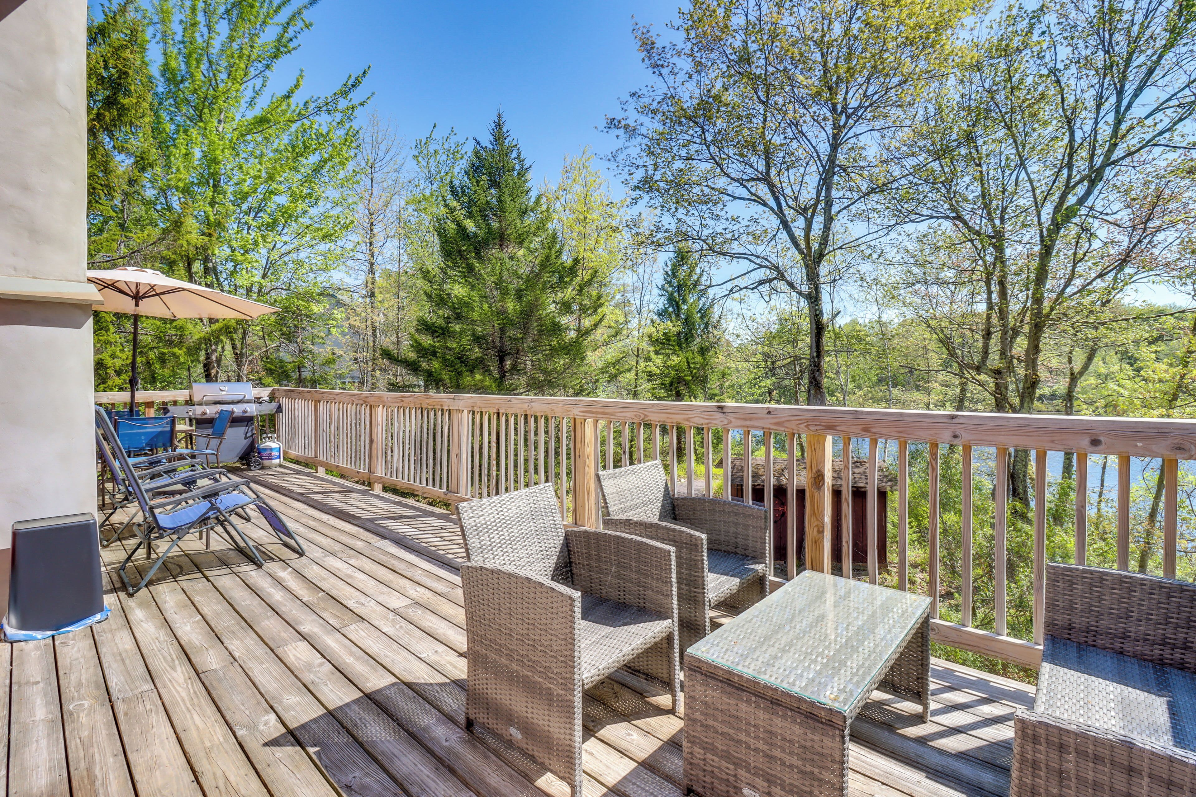 A wooden deck with wicker furniture and a table, overlooking a forested area.