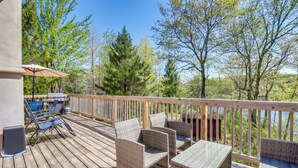 Une terrasse en bois, dotée de meubles en osier et d’une table, qui offre une vue sur une zone boisée.
