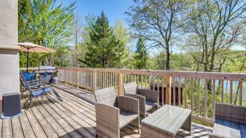 A wooden deck with wicker furniture and a table, overlooking a forested area.