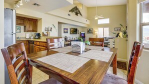 Uma ampla área de refeições com mesa e cadeiras de madeira, cozinha ao fundo e um ventilador de teto.