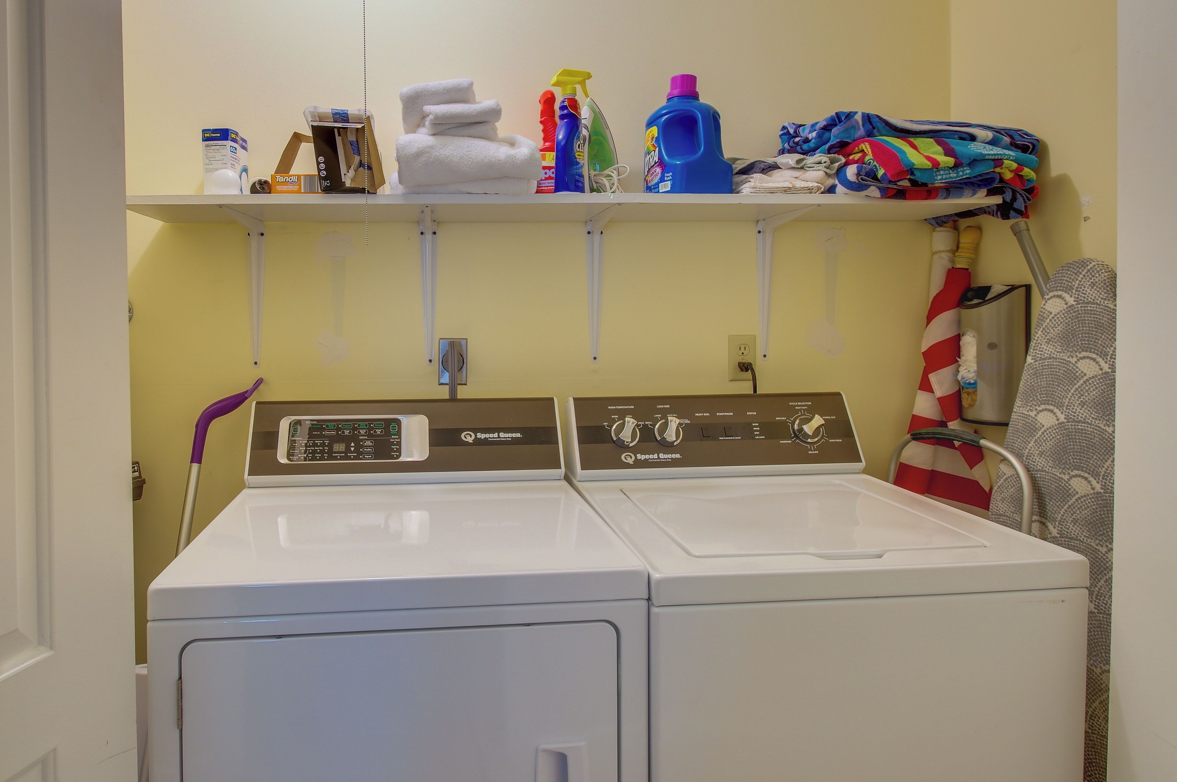A laundry area with two front-loading washing machines, a shelf with cleaning supplies, and folded towels.
