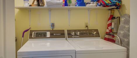 A laundry area with two front-loading washing machines, a shelf with cleaning supplies, and folded towels.