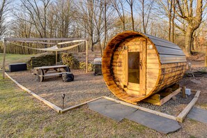 A wooden sauna structure with a bench and a table, surrounded by a stone wall and trees. - Pearl Creek House w/ Barrel Sauna & Fire Pit! (Purling)