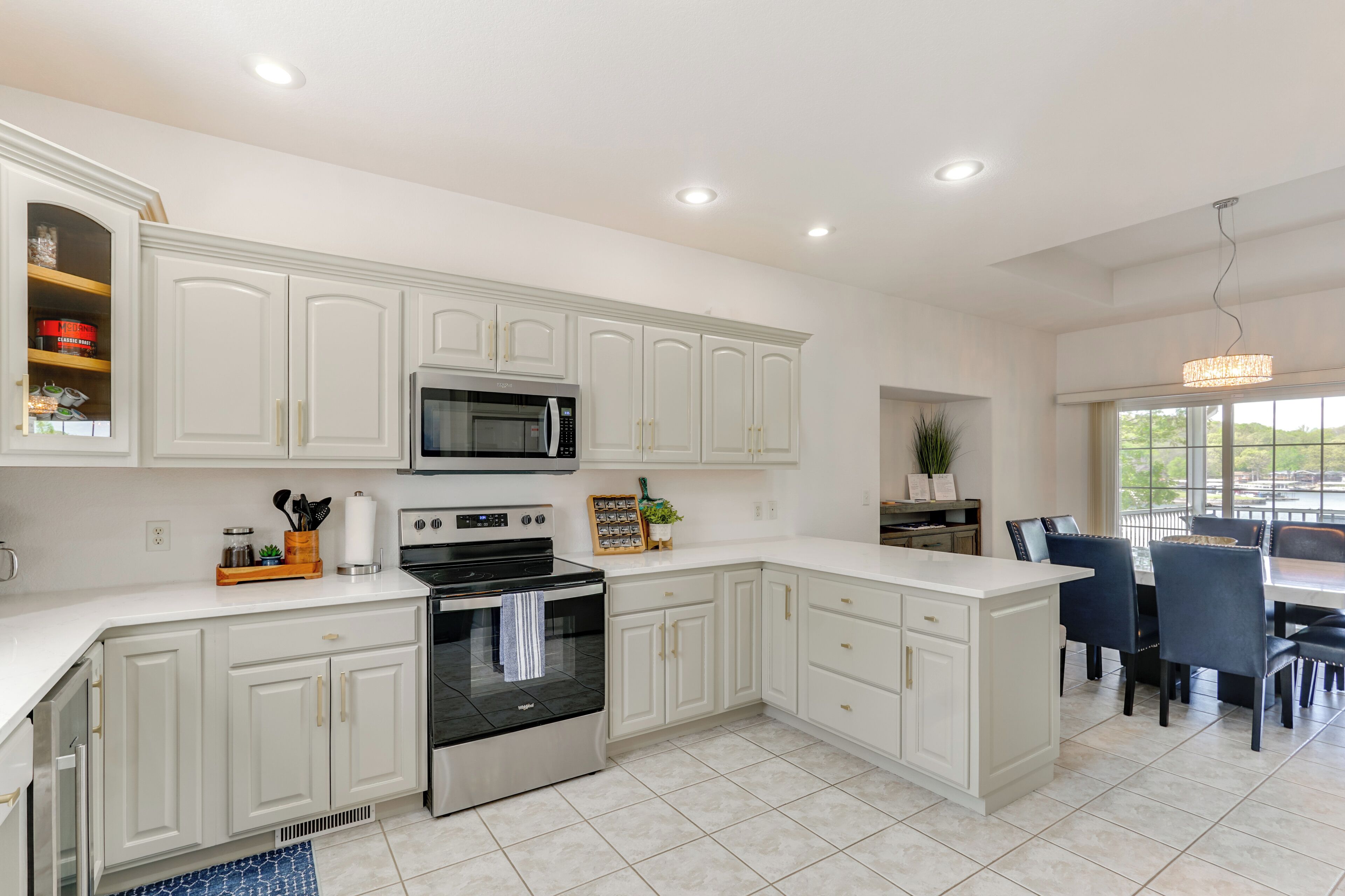 A modern kitchen with white cabinetry, a built-in microwave, and an oven. There is a dining area with a table and chairs.