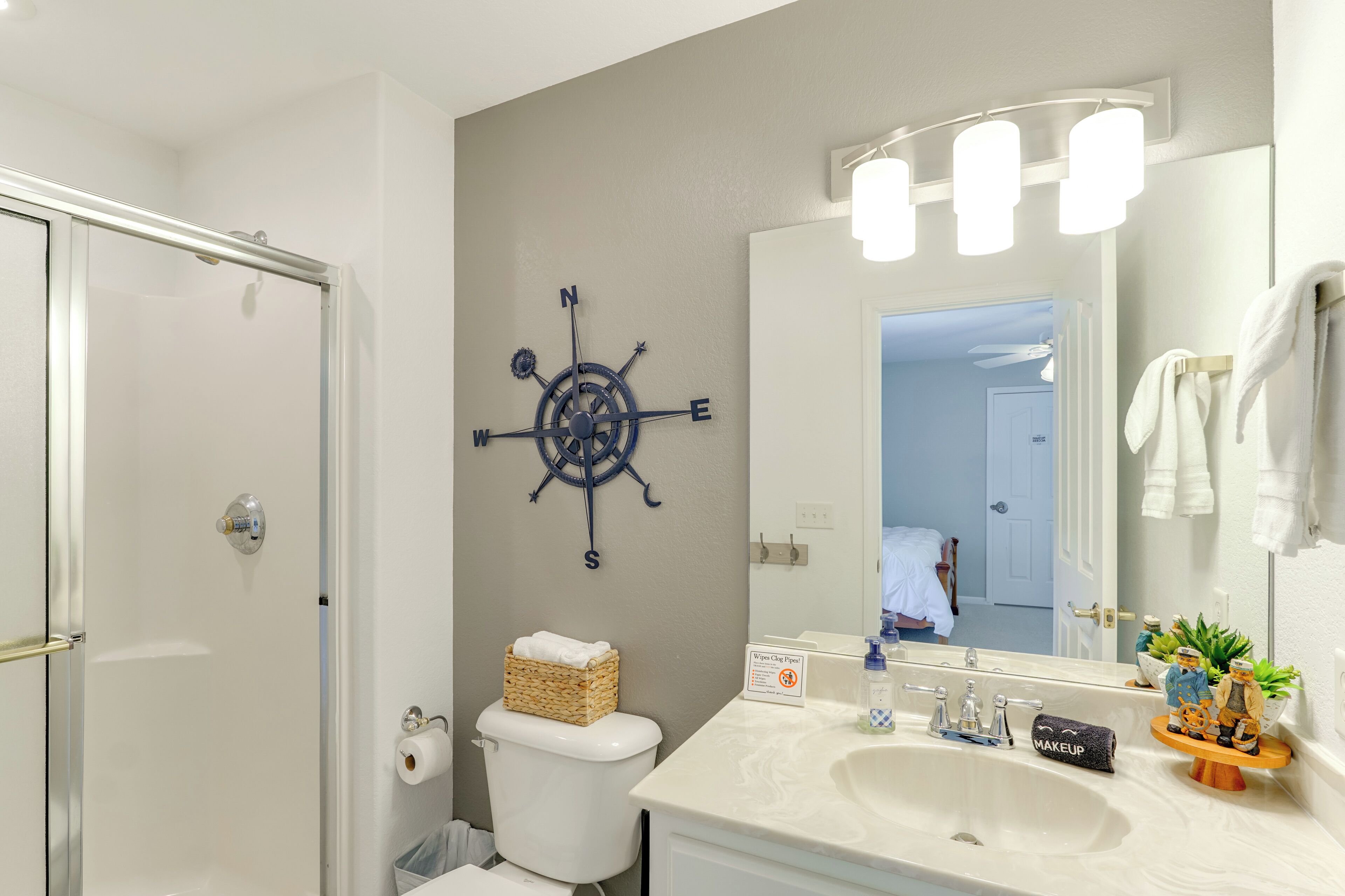 A bathroom with a white sink, a mirror, a compass wall decoration, and a shower area.