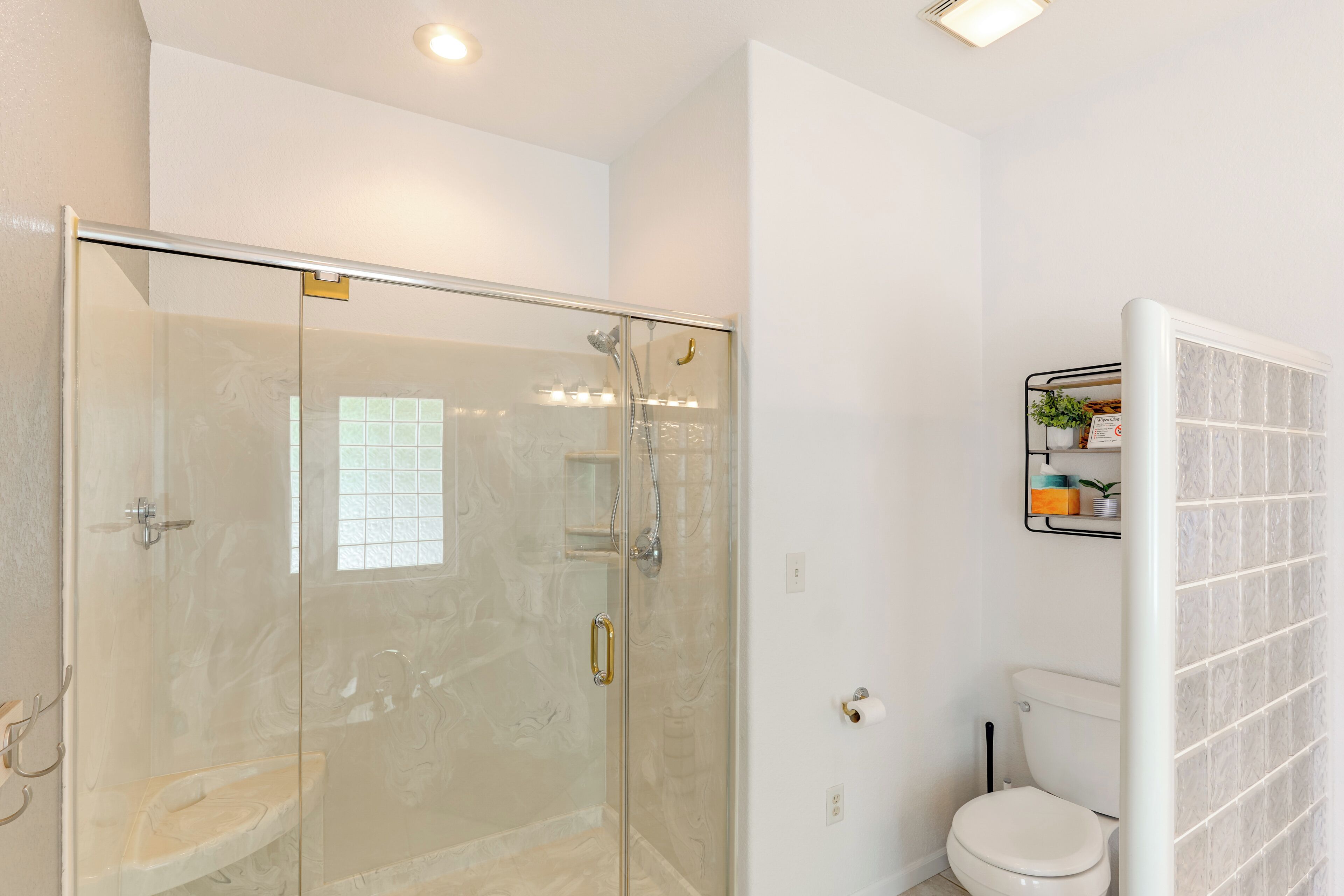 Un baño moderno con ducha de vidrio, inodoro y un estante pequeño con artículos de aseo.