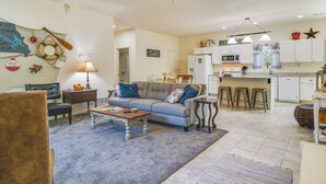 Un salón amplio con un sofá gris, una mesa de centro de madera y una zona de comedor, con una cocina al fondo.