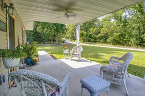 A covered porch with wicker furniture, potted plants, and a view of a green landscape.