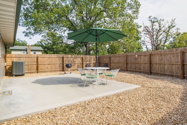 A patio area with a concrete floor, a round table with chairs, and a green umbrella.